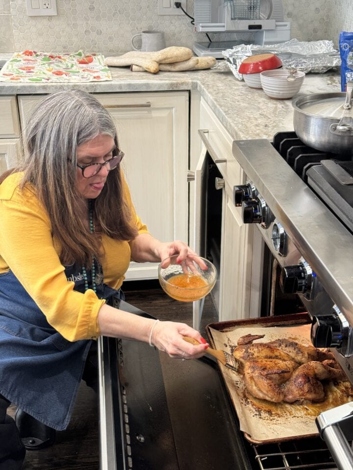 woman with yellow top basting chicken in oven 