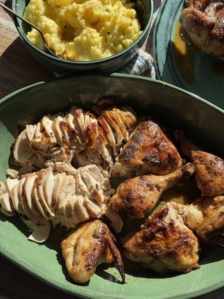 carved chicken on green platter next to bowl of mashed potatoes