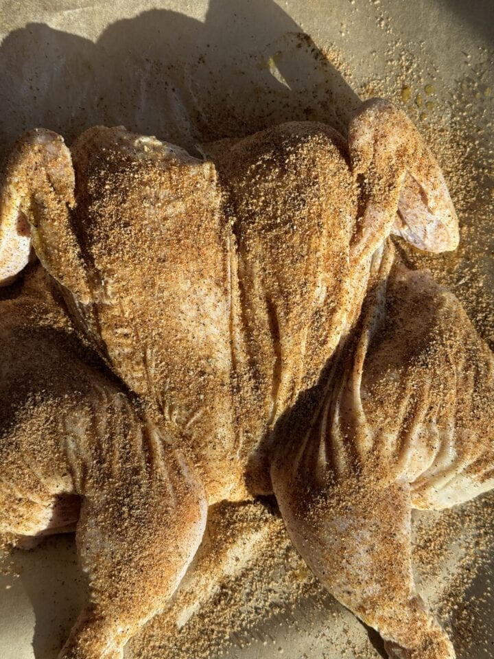 raw spatchcock chicken covered in spice blend on parchment line baking pan