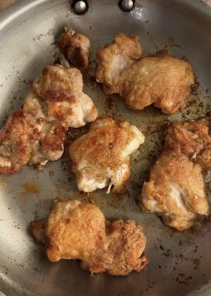 crispy chicken thighs cooking in a stainless steel pans