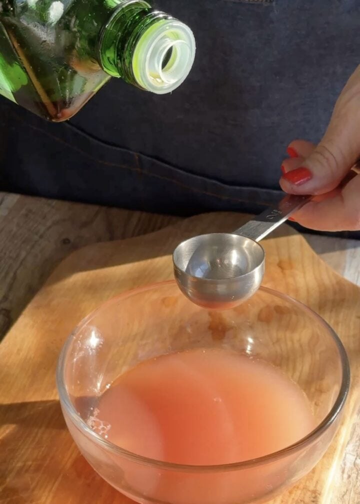 measuring olive oil over a clear bowl with grapefruit juice