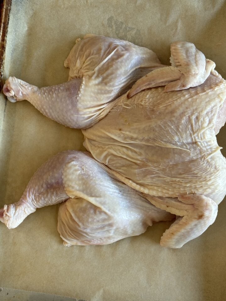raw naked spatchcock chicken on parchment lined baking pan