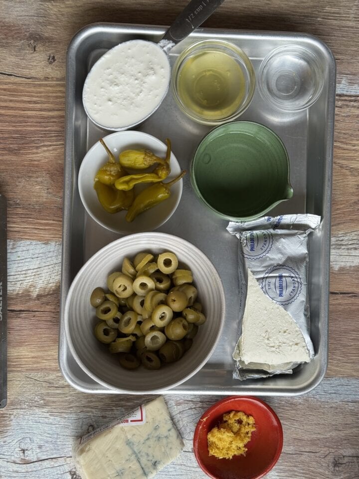 the ingredients for dirty martini dip in small bowls on a baking sheet