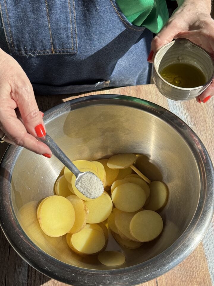 salt on potato rounds in a metal bowl