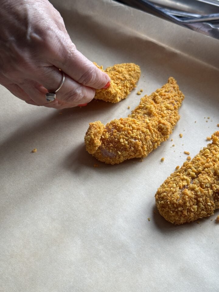 teri placing breading chicken fingers on a baking sheet