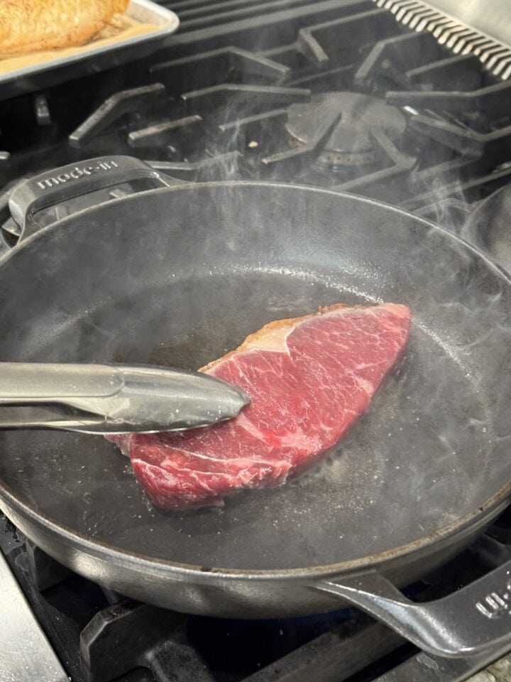 steak cooking in a cast iron pan