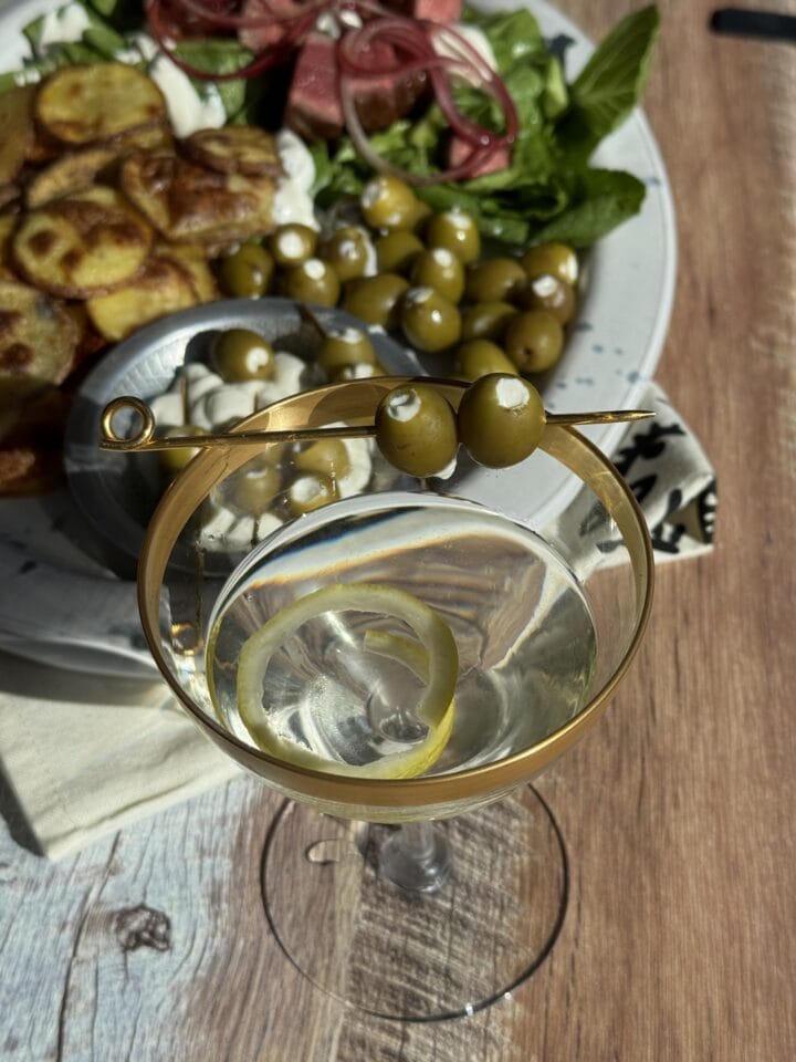 dirty martini with two olives on a toothpick and a salad in the background