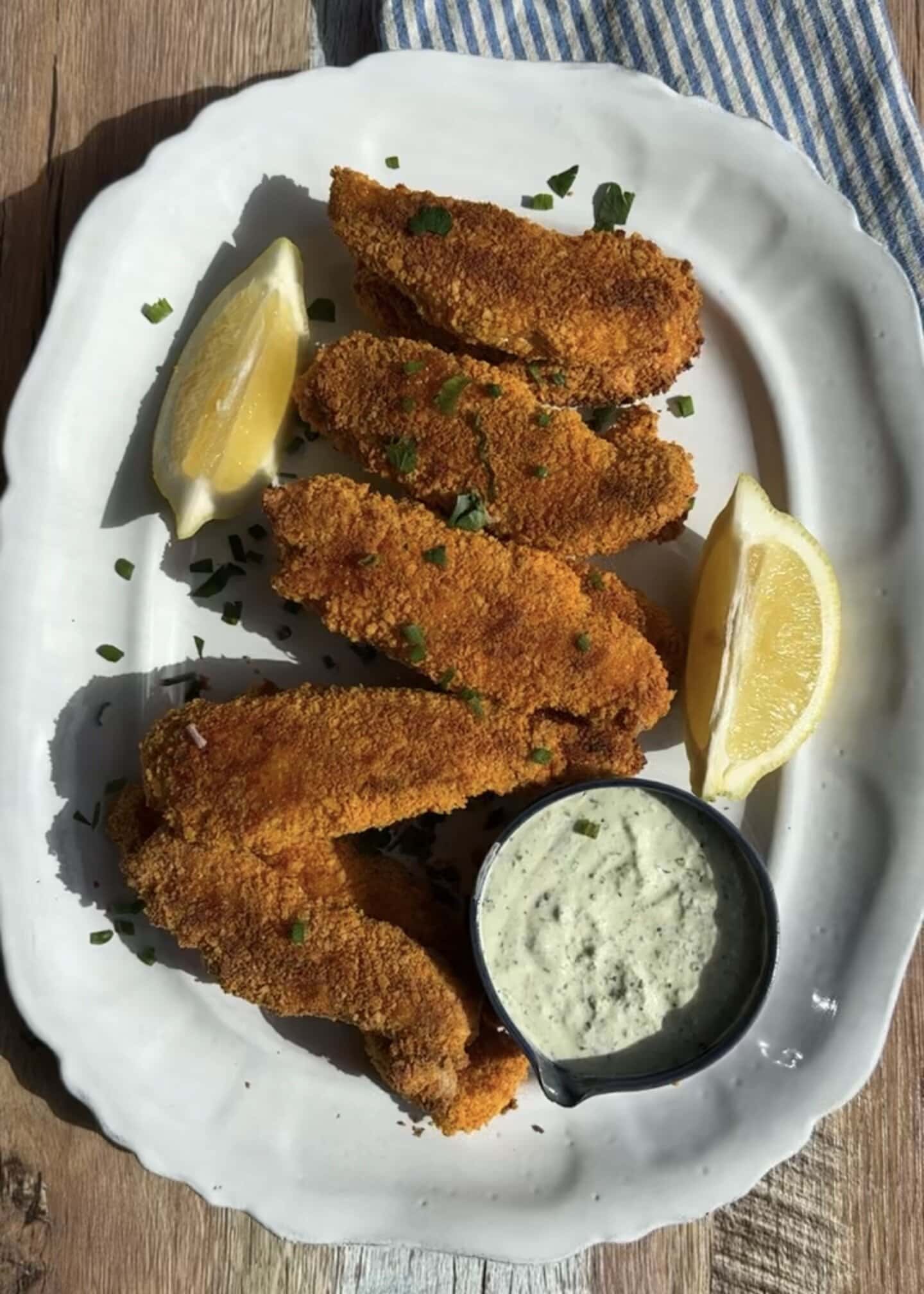baked chicken fingers on a white platter with dip and lemon wedges around it