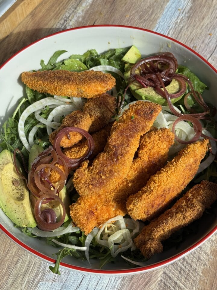 baked chicken fingers on a salad in a white bowl