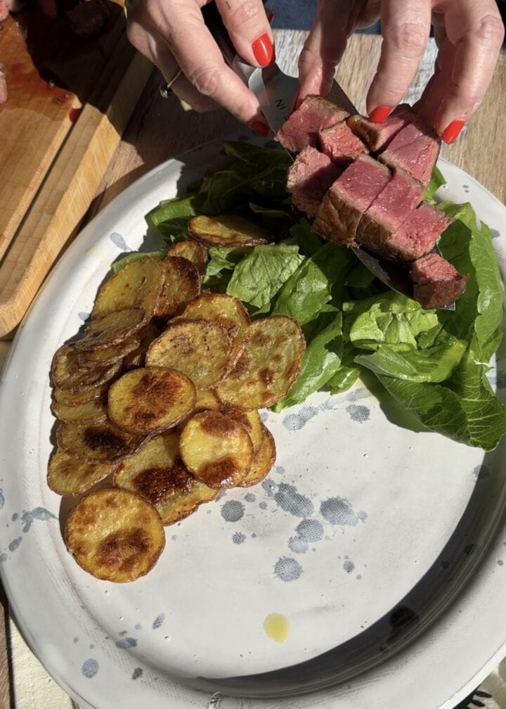 adding cubed steak to a platter with lettuce and crispy potato rounds