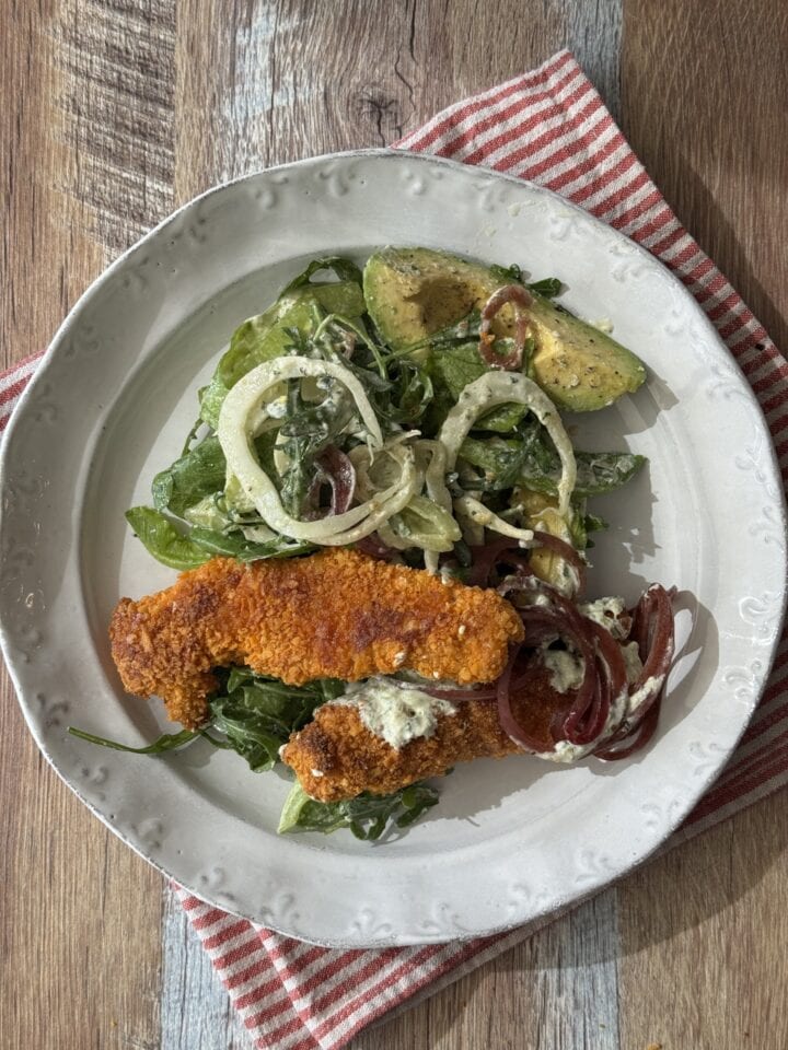 baked chicken fingers on a white plate with salad next to it