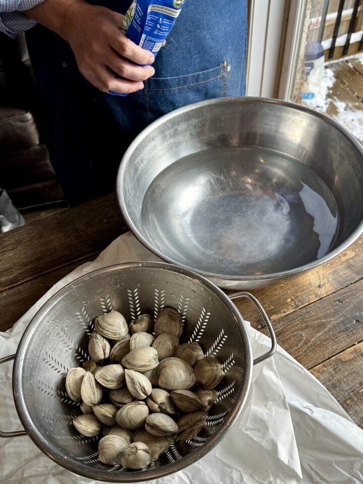 clams in a strainer next to a large bowl of water