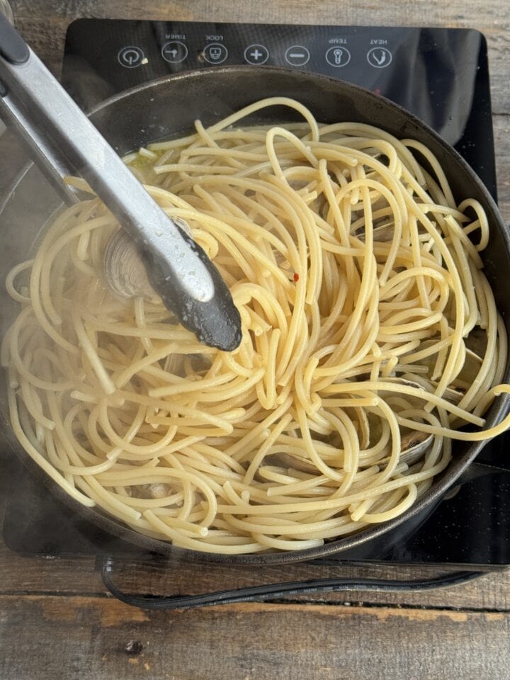 linguine pasta in a pan with tongs in it