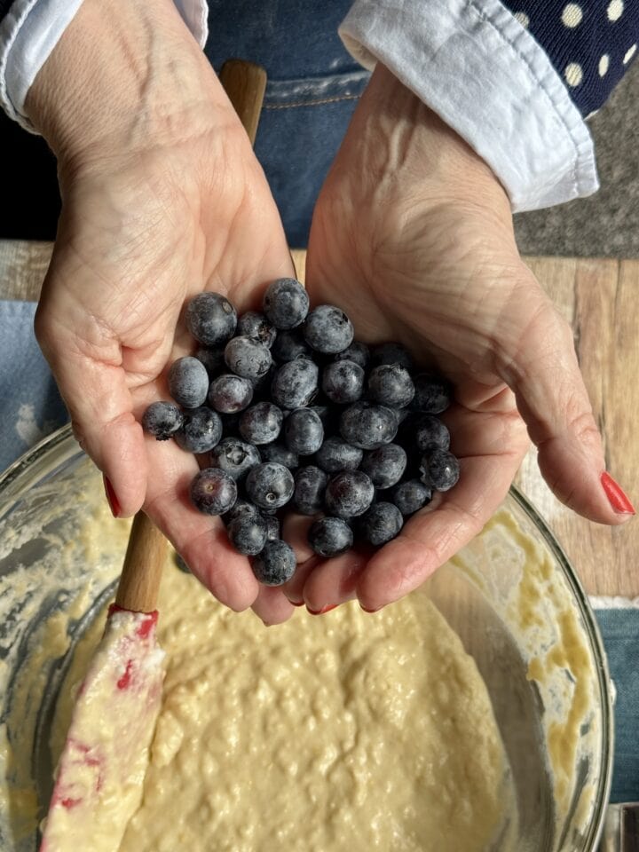 teri holding blueberries above the waffle batter in a glass bowl