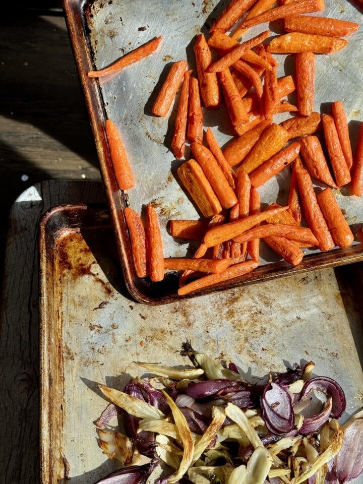 roasted carrots on a sheet pan pouring onto a sheet pan with fennel and onion