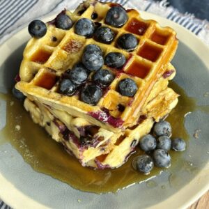 a stack of blueberry waffles with blueberries and syrup on top