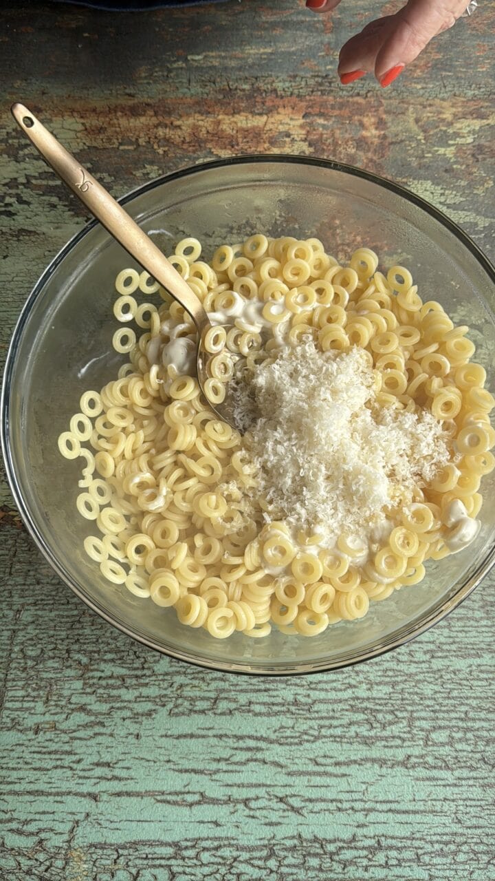 pasta and parmesan cheese in a glass bowl with a wooden spoon