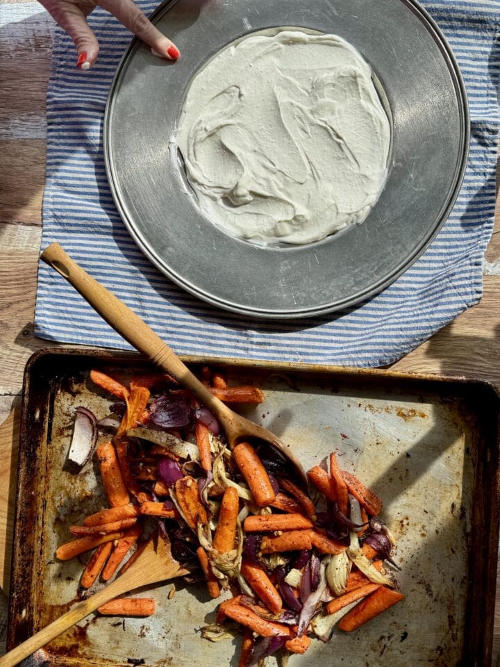 roasted vegetables on a sheet pan next to a platter with labneh on it