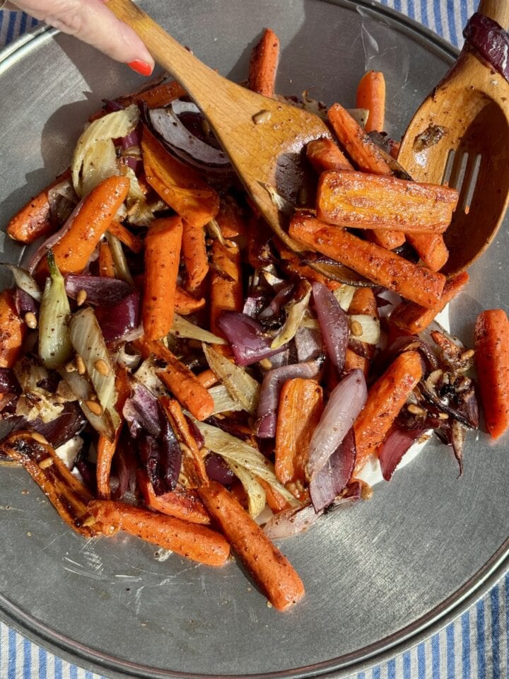wooden spoons placing roasted vegetables on a silver platter