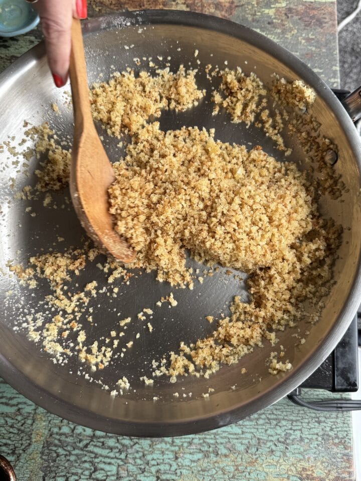 toasted breadcrumbs in a stainless steel pan with a wooden spoon