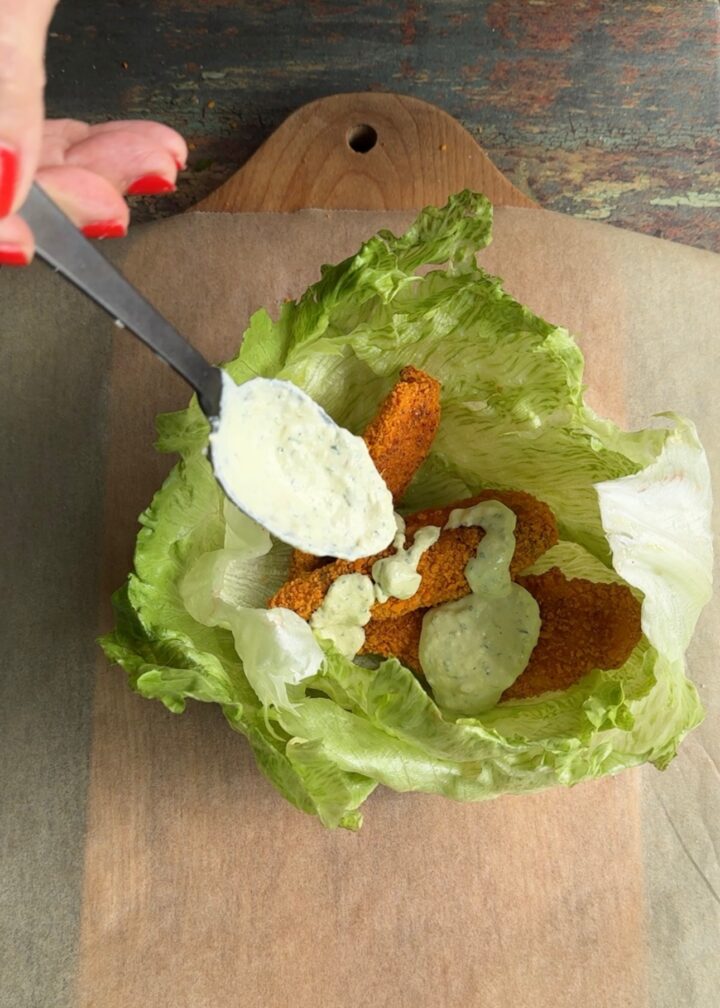 dressing on top of chicken fingers in a lettuce wrap