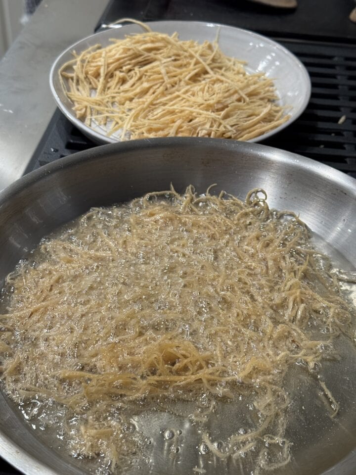 tortilla strips frying in oil in a stainless steel pan