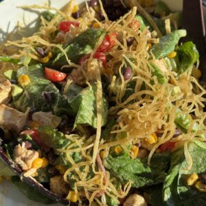 southwest chicken salad in a white bowl with wooden spoons