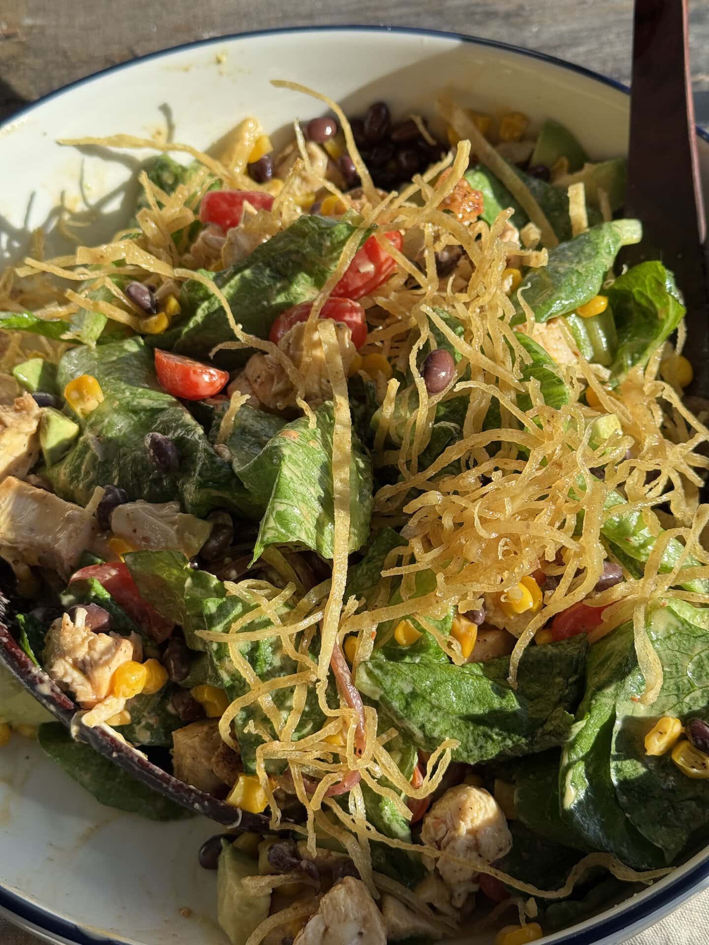 southwest chicken salad in a white bowl with wooden spoons