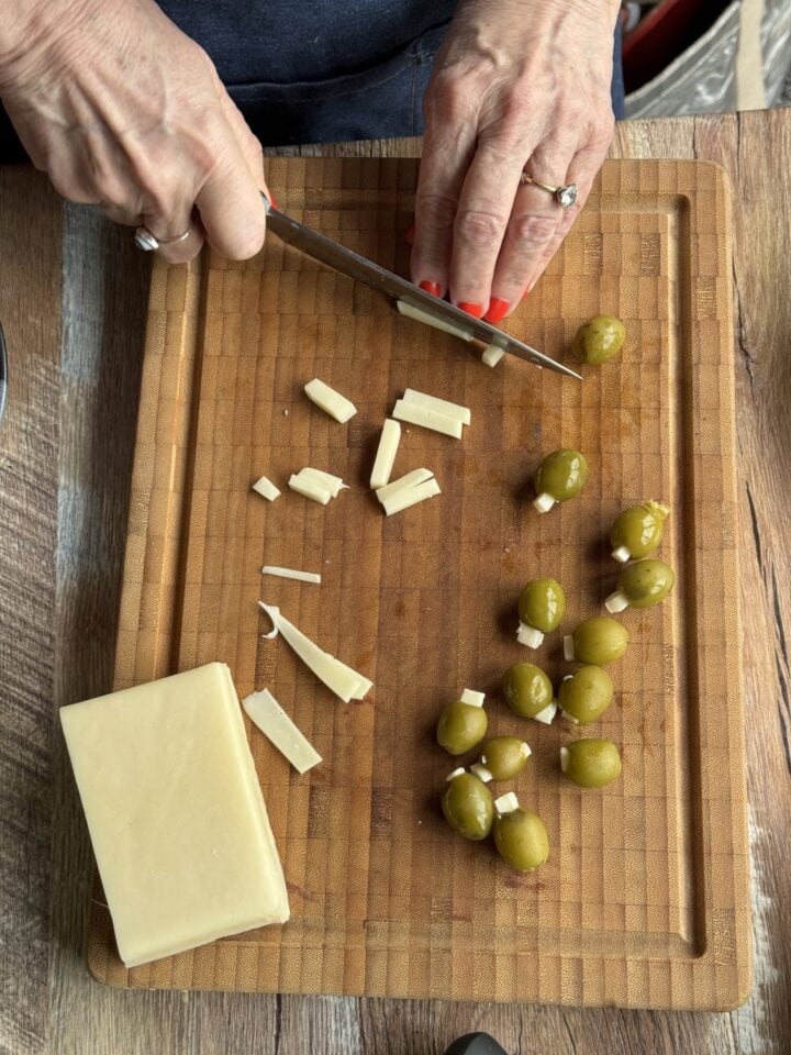 teri slicing fontina cheese on a wooden cutting board with olives next to it