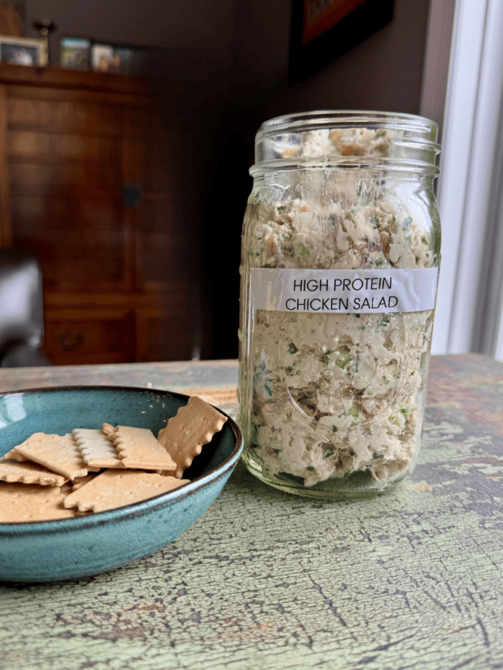 high protein chicken salad in a jar with a bowl of crackers next to it