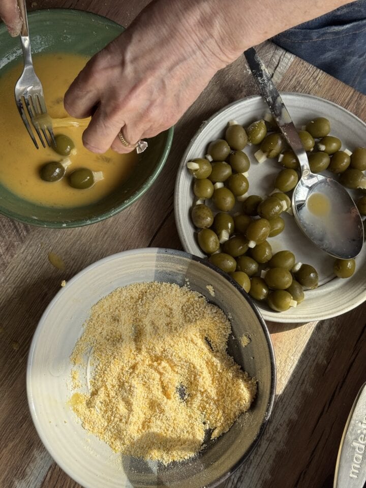 a bowl of eggs, a plate with cornmeal, and a plate with stuffed olives on a table
