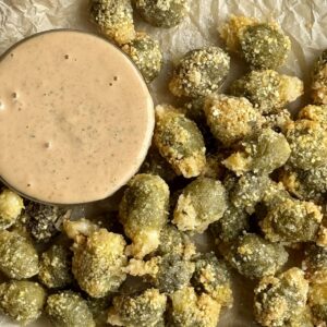 fried olives on parchment paper with a bowl of dipping sauce next to them