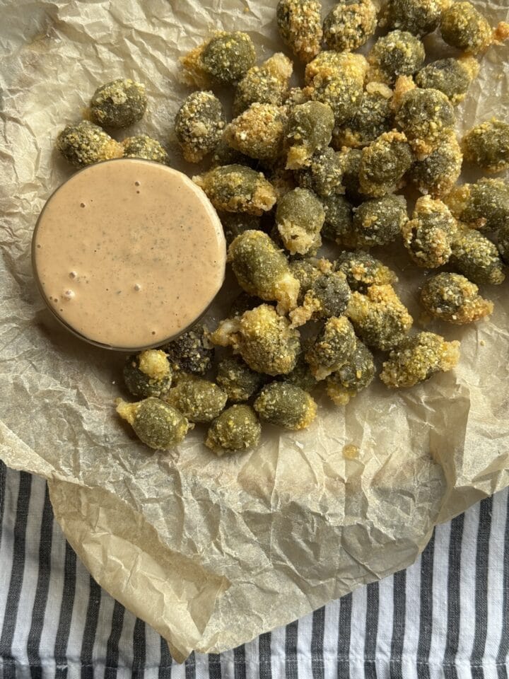 fried olives on parchment paper with a bowl of dipping sauce next to them