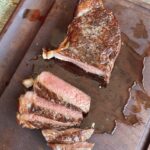 a reverse sear steak on a wooden cutting board with a few slices cut