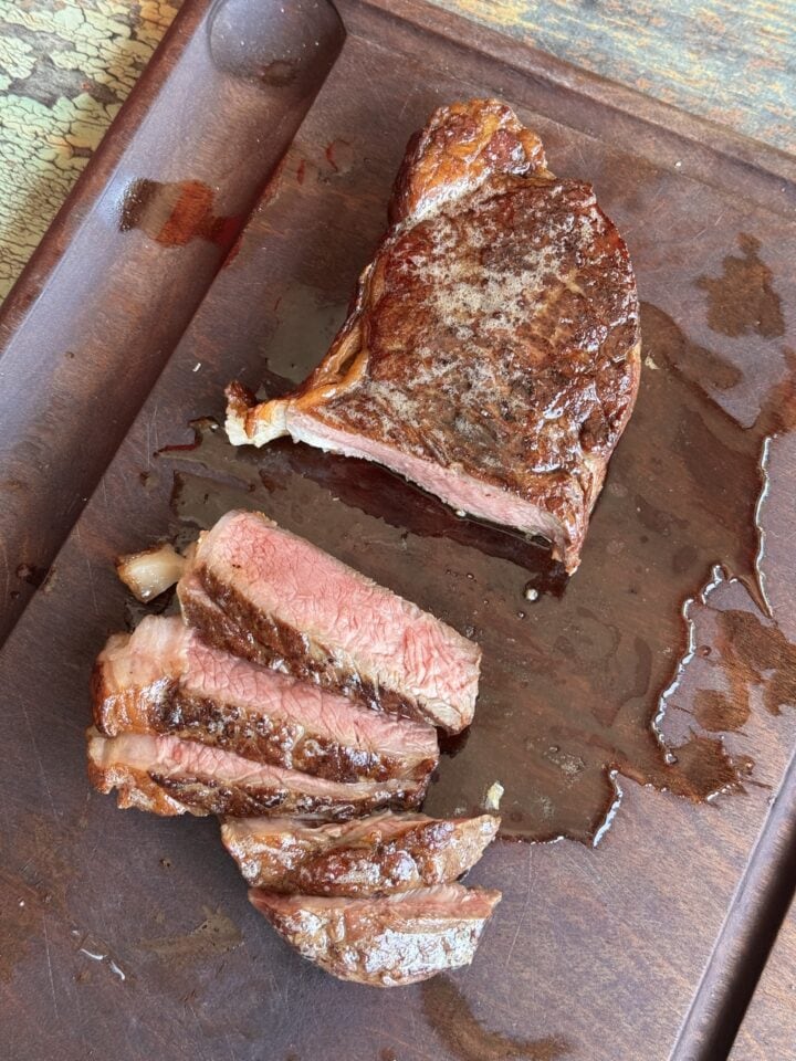 a reverse sear steak on a wooden cutting board with a few slices cut