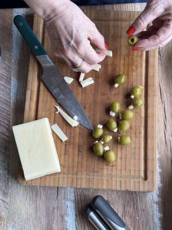 teri stuffing an olive with fontina cheese with a bunch of stuffed olives on a cutting board