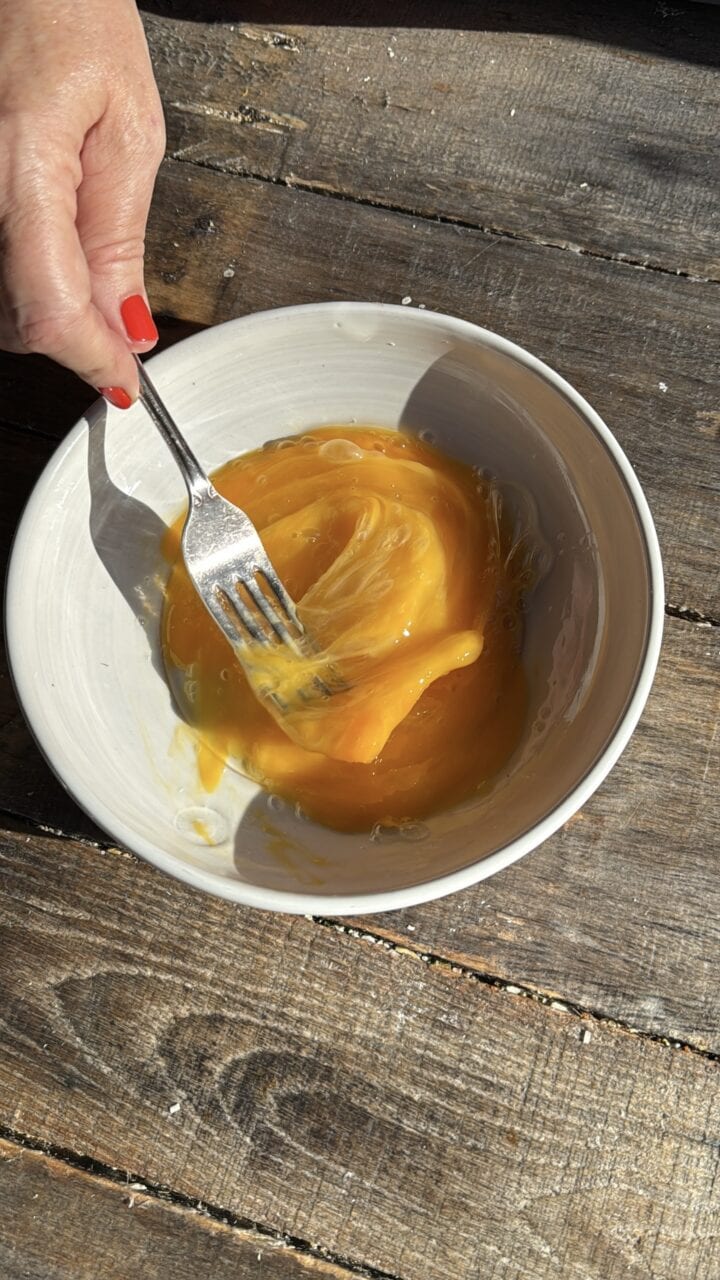 a hand whisking a fork in a bowl of eggs