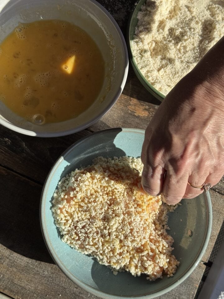 flour, eggs, and panko in three bowls with a chicken cutlet in the panko