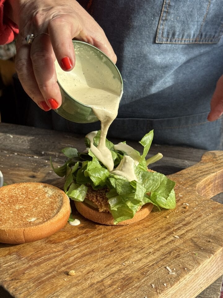 teri pouring dressing from a small bowl onto a chicken caesar sandwich