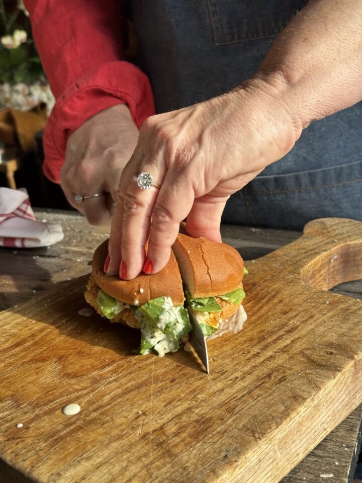 teri cutting a chicken caesar salad sandwich in half on a cutting board