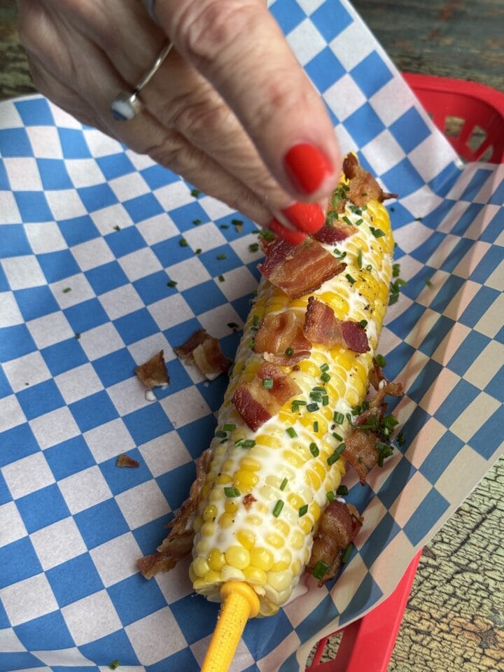 teri sprinkling bacon on a corn cob