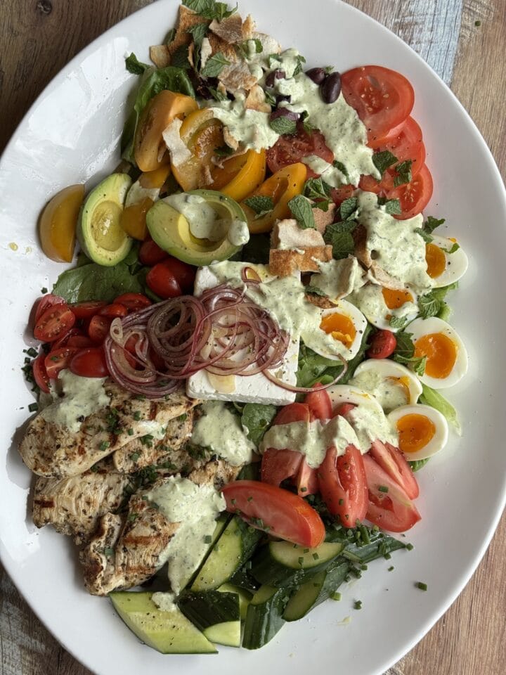 mediterranean chicken salad on a white platter with dressing drizzled on top