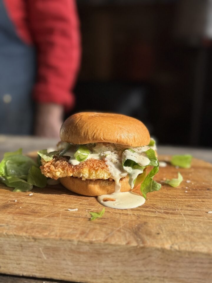 fried chicken caesar salad sandwich on a wooden cutting board