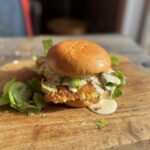 fried chicken caesar salad sandwich on a wooden cutting board