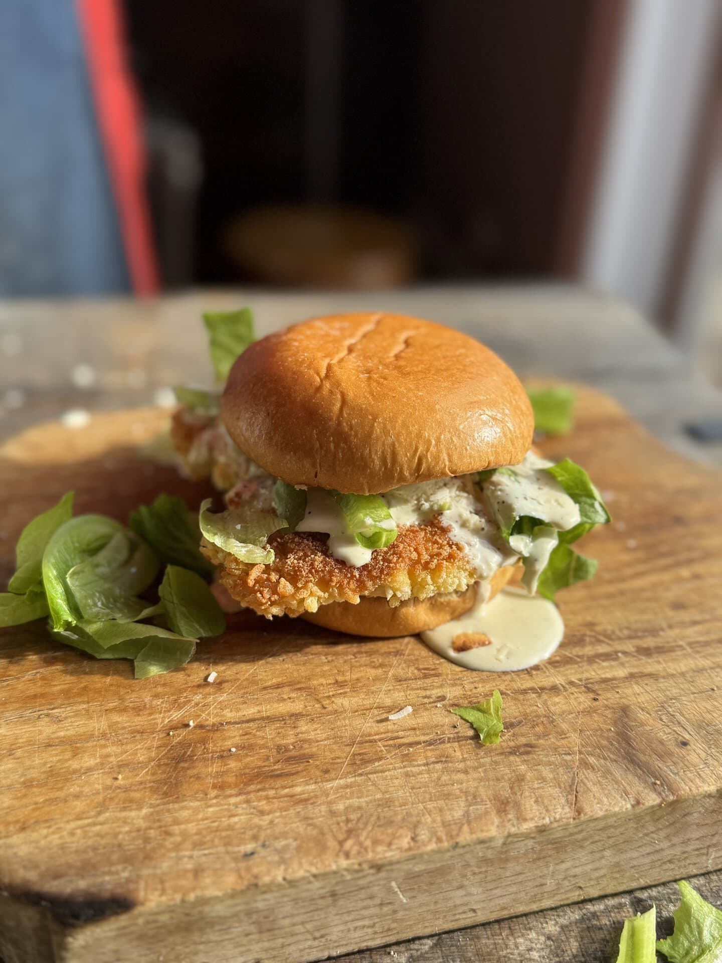 fried chicken caesar salad sandwich on a wooden cutting board