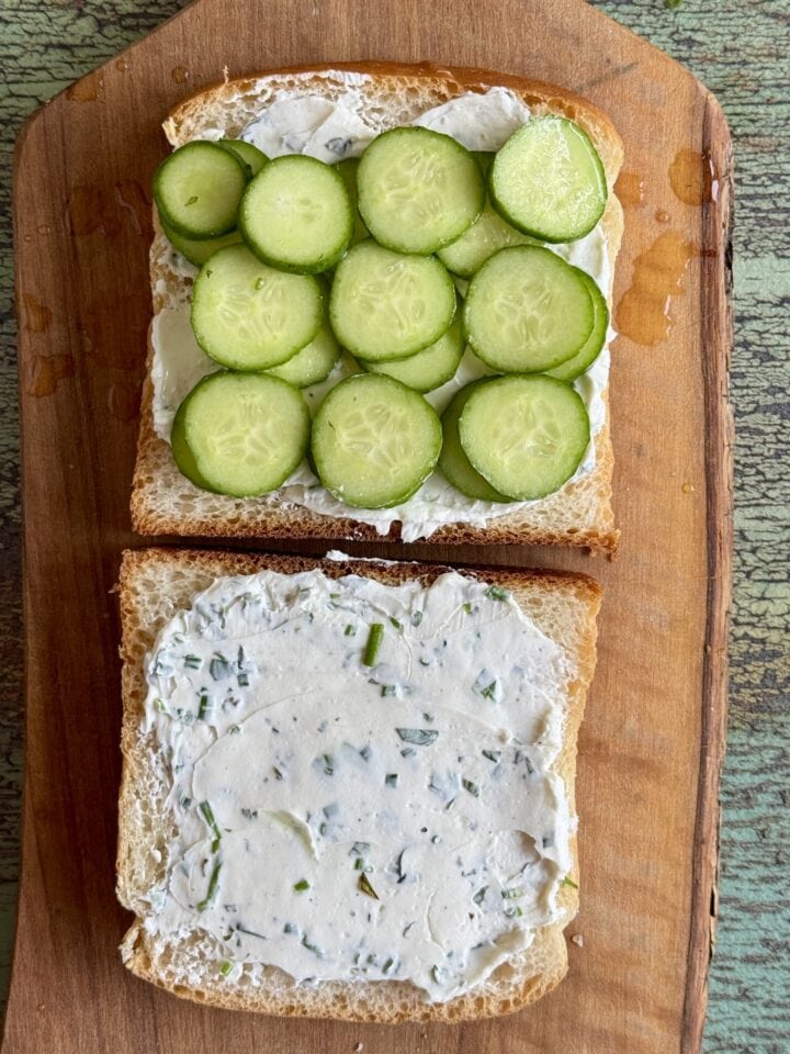 an open face cucumber sandwich on a wooden cutting board