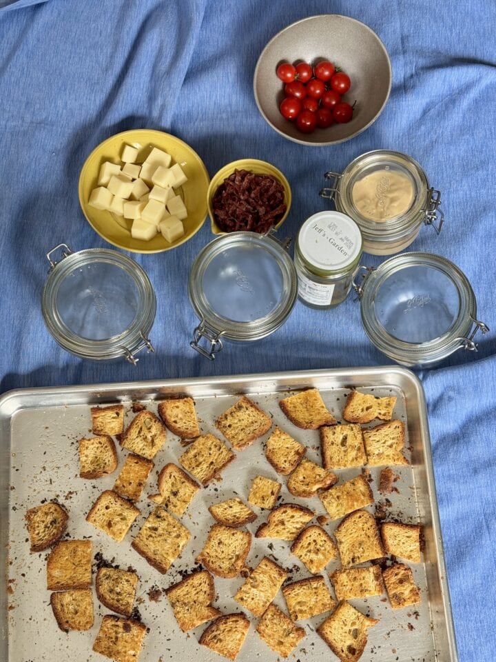 ingredients for a grinder salad in small bowls with a sheet pan of croutons next to them