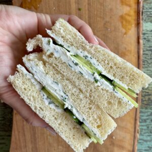 a cucumber sandwich held in a hand above a wooden cutting board