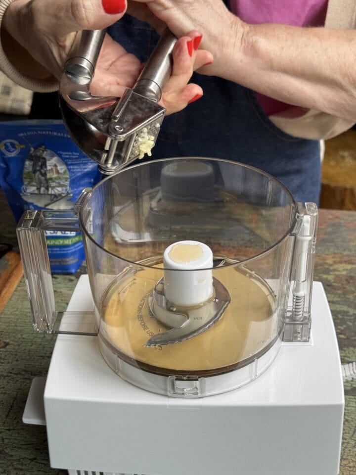 teri adding pressed garlic to a food processor
