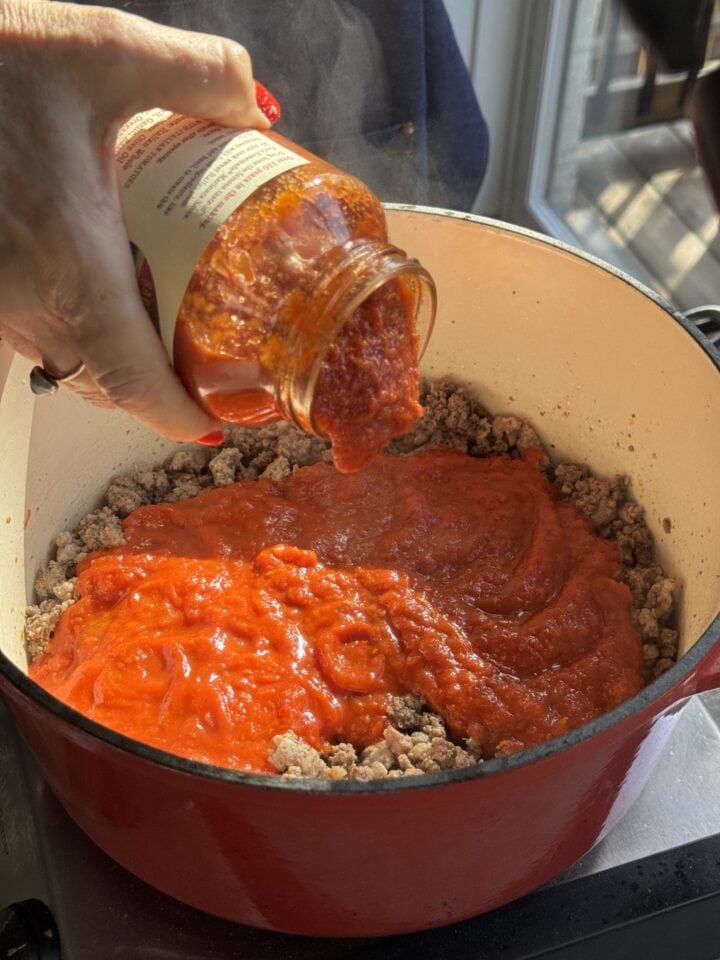 sauce pouring into a dutch oven with ground meat in it